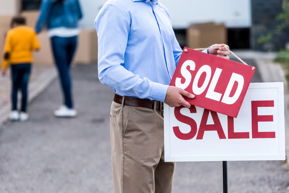 Real estate agent holding a Sold sign over a For Sale sign outside a home